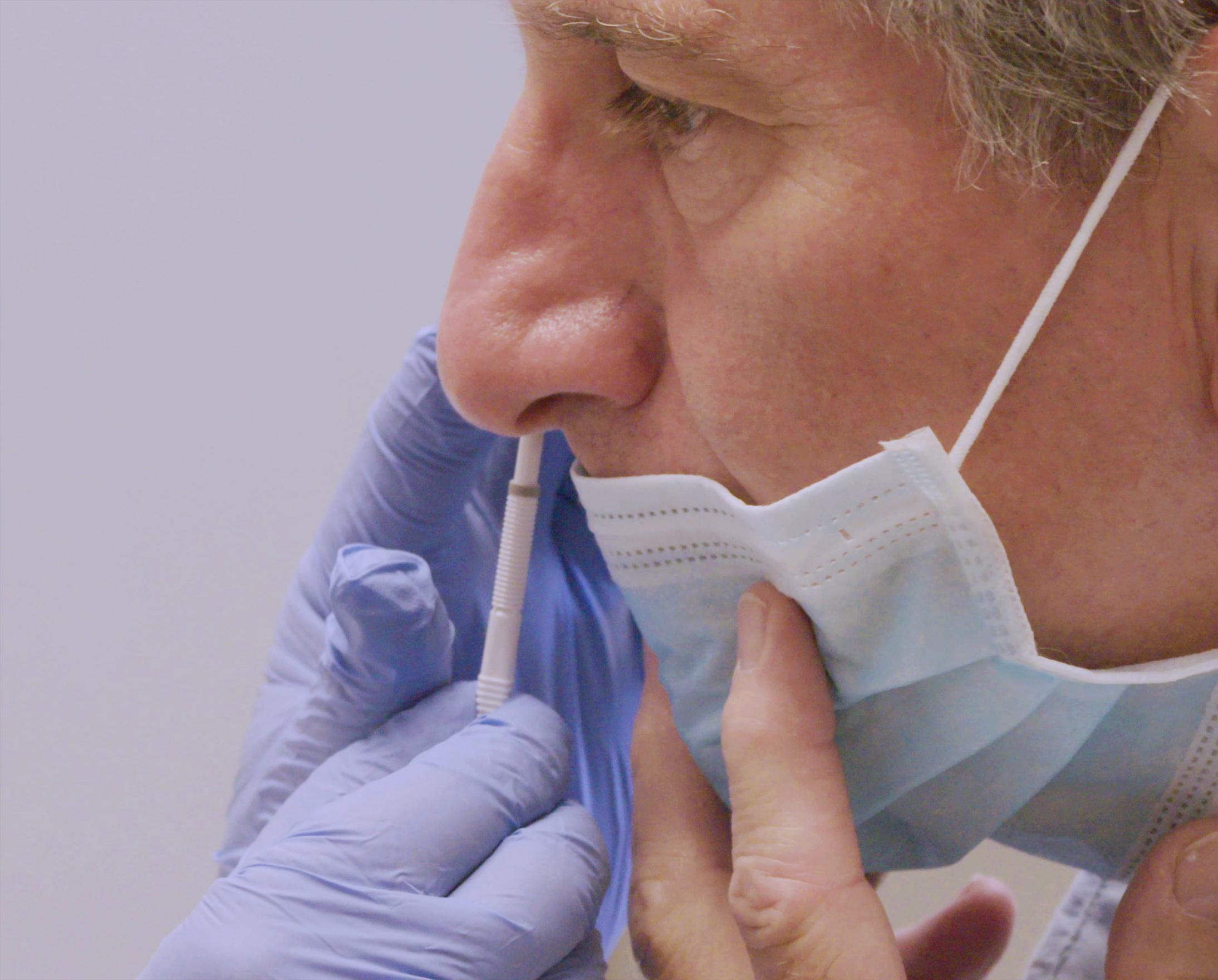 A gloved hand swabs a man's nostril with a Cue Wand